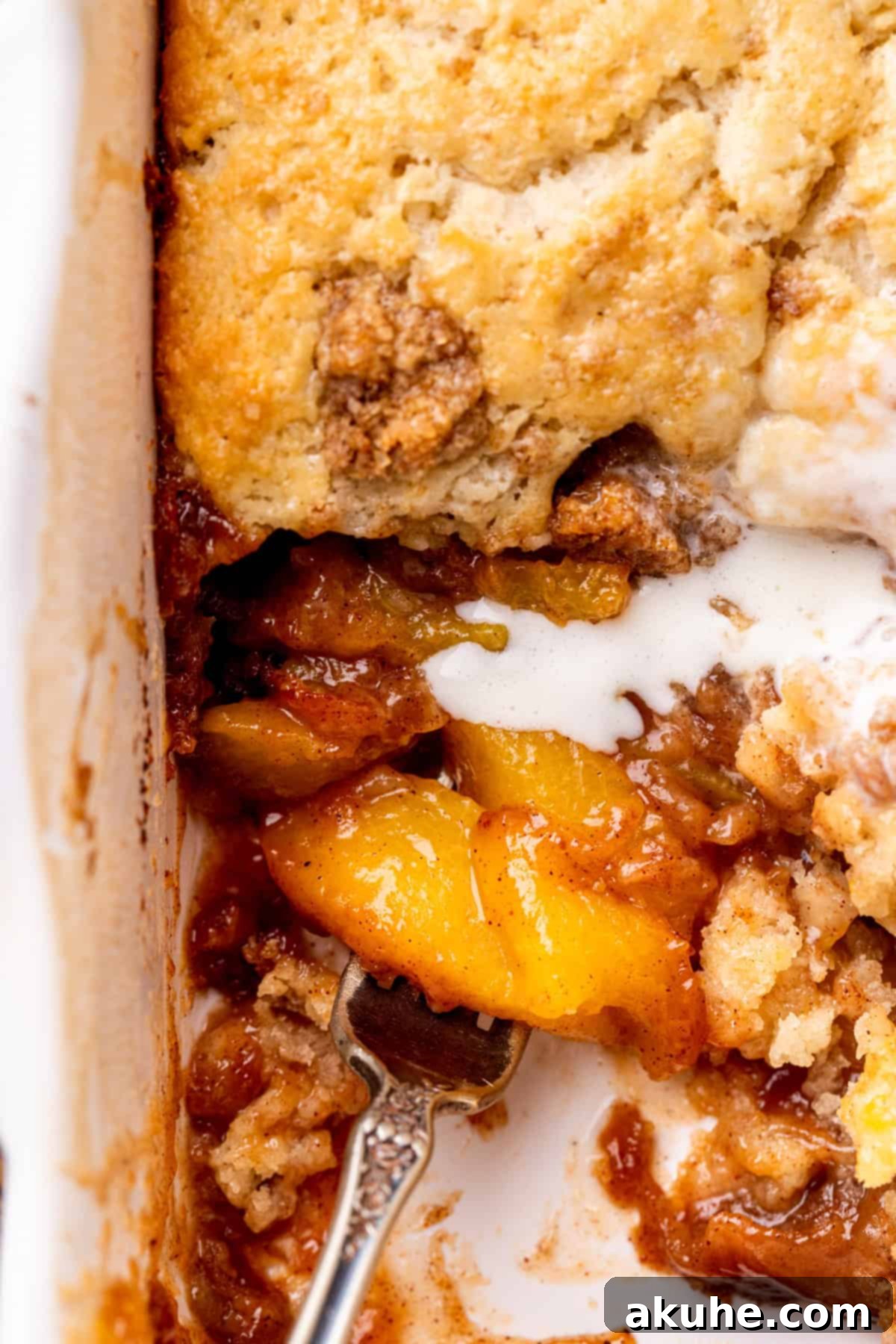 A fork taking a bite of cinnamon peach cobbler, showing the layers of biscuit and peach filling.