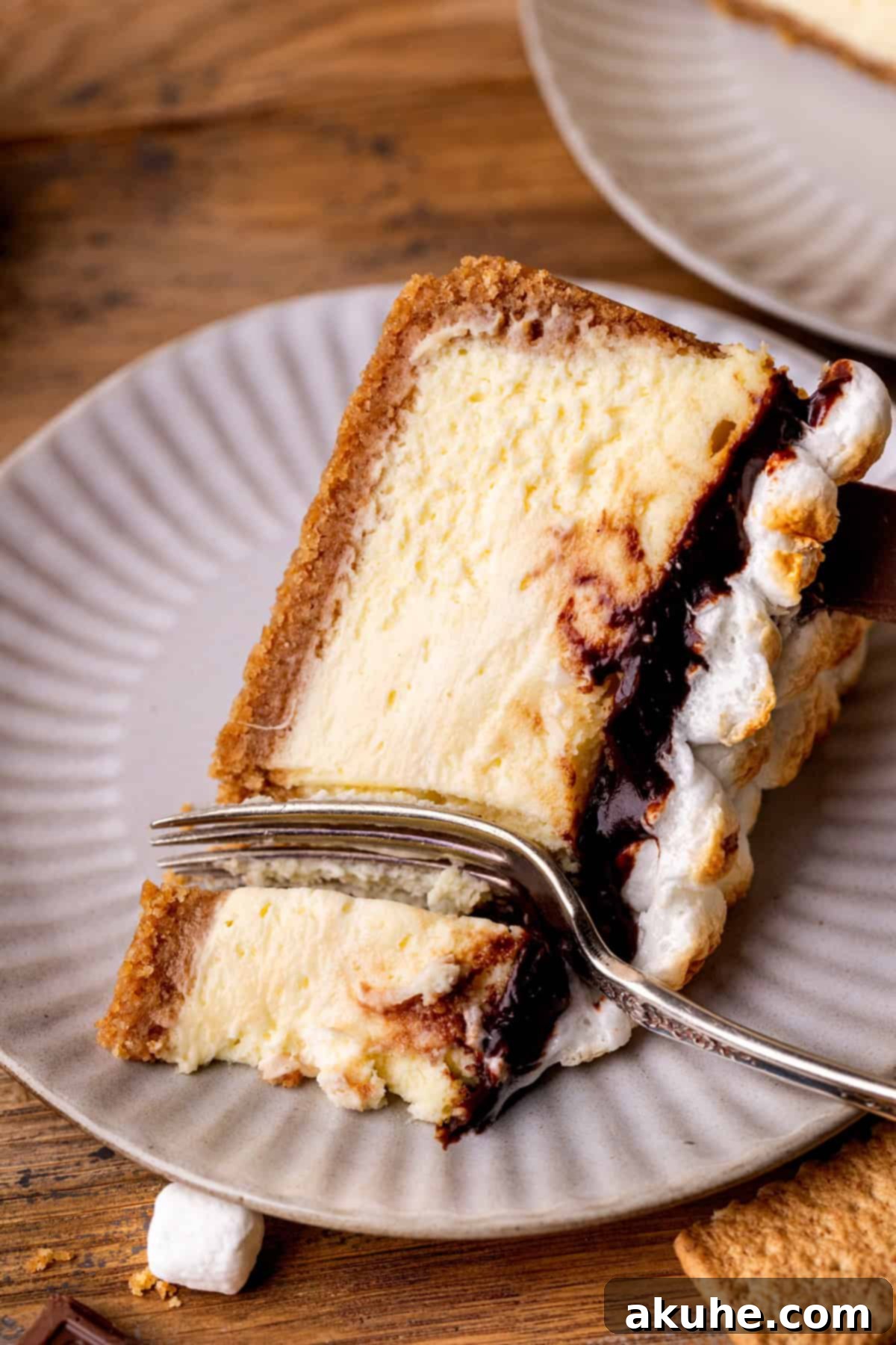 One slice of S'mores cheesecake on a plate with a fork inserted, ready to be eaten.