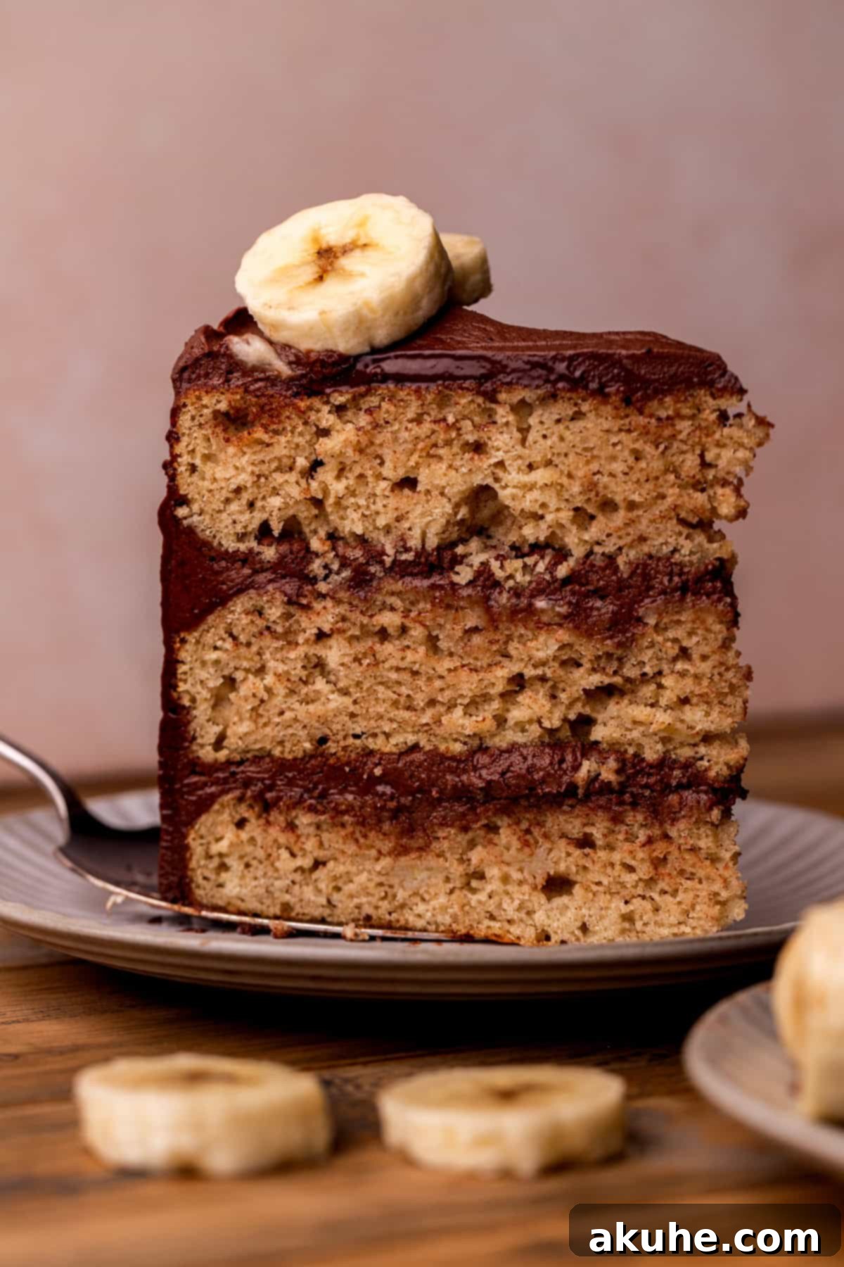 Decadent Banana Chocolate Dream Cake 2 A perfectly sliced piece of moist banana cake generously topped with rich chocolate cream cheese frosting, resting on a white plate, ready to be enjoyed.
