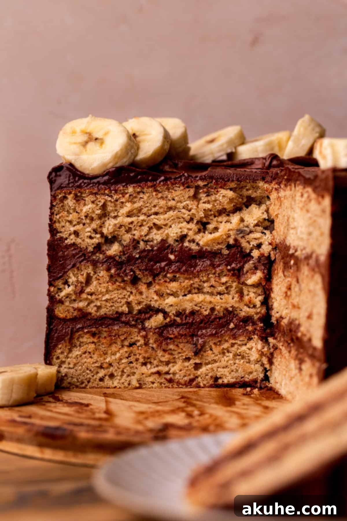 Decadent Banana Chocolate Dream Cake 11 A stunning side view of the three-layer banana cake with chocolate frosting on a rustic wood board, perfectly decorated.
