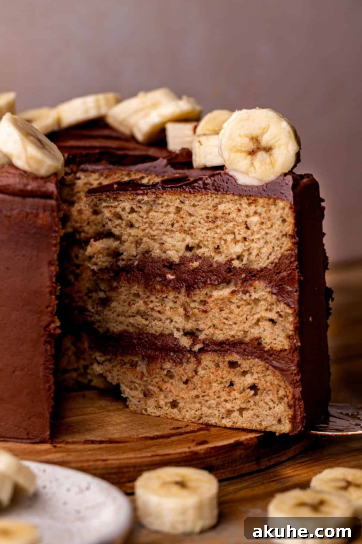 Decadent Banana Chocolate Dream Cake 9 A hand gently removing a slice from a beautifully frosted banana cake, revealing its moist layers.
