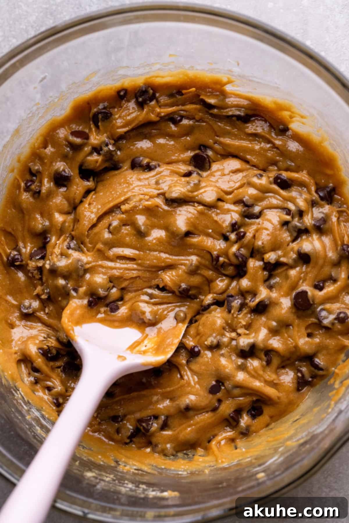 Decadent Caramel Cookie Bars 6 Rich cookie dough, a blend of dry and wet ingredients, in a glass mixing bowl.