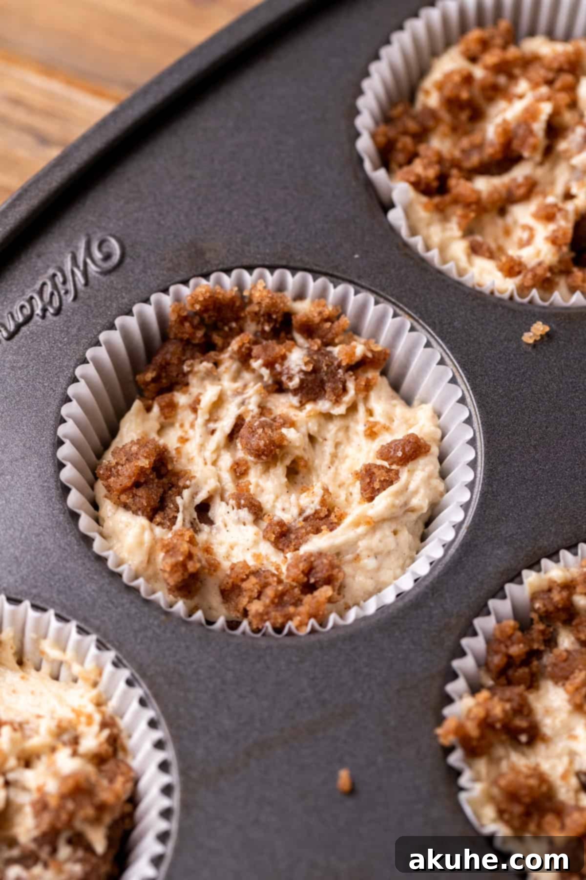Cupcake pan showing liners filled with layered cupcake batter and cinnamon swirl, ready for baking.