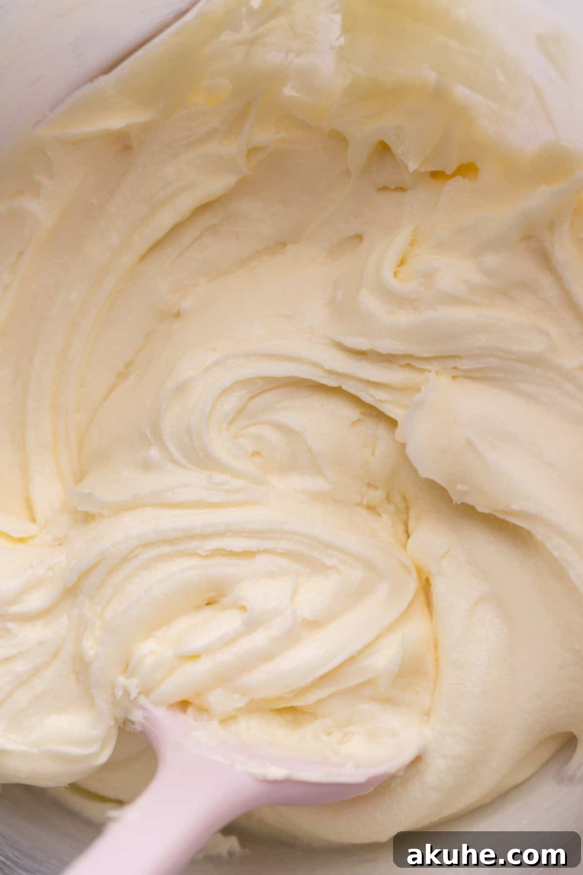 Smooth and creamy cream cheese frosting in a clear glass bowl, showcasing its ready-to-pipe consistency.
