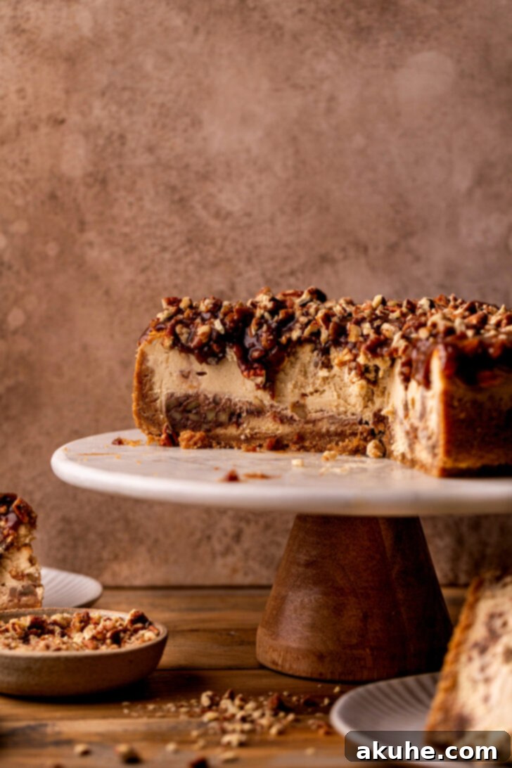 Pecan Pie Cheesecake 9 Full pecan pie cheesecake on a cake stand, side view, showing its height and topping.