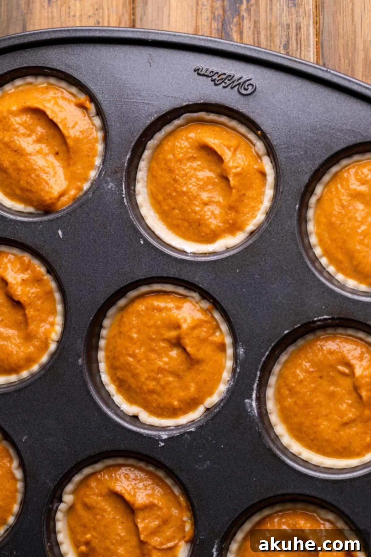 Pumpkin batter carefully scooped into pie crusts in a muffin pan, ready for baking.