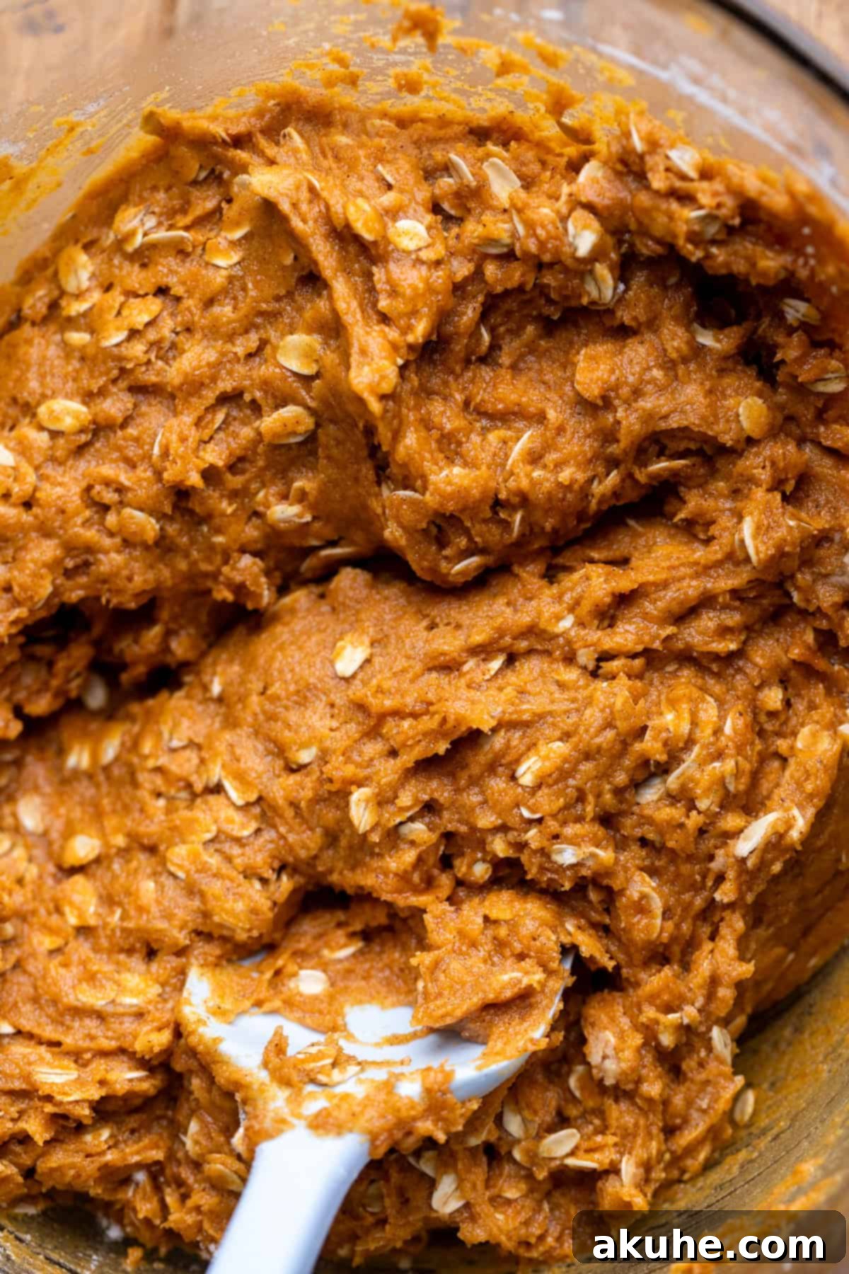 Spiced Pumpkin Oatmeal Cream Pies 4 Pumpkin oatmeal cookie dough in a clear glass bowl, showcasing its rich orange color and visible oat flakes.