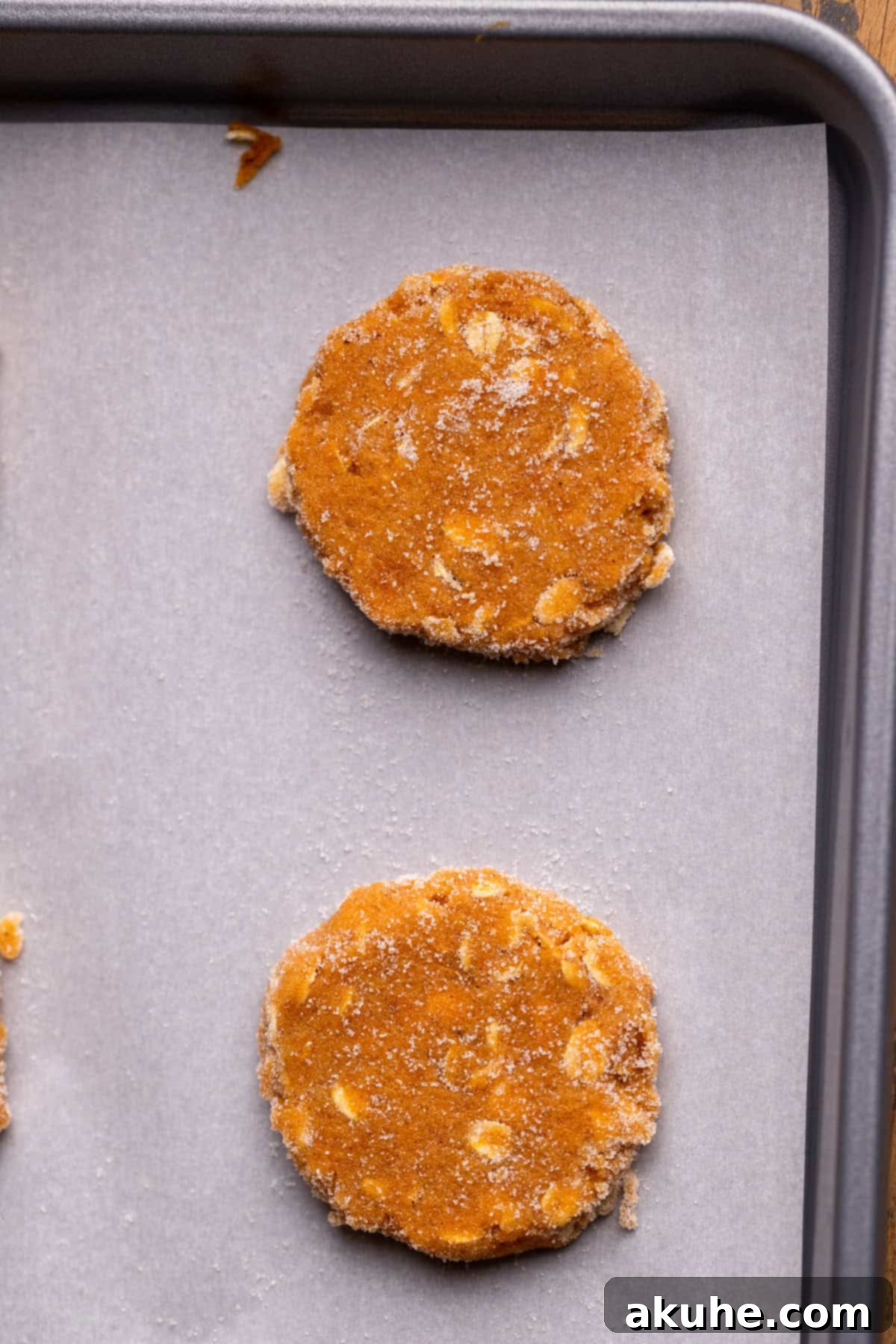 Spiced Pumpkin Oatmeal Cream Pies 5 Uniformly shaped pumpkin cookie dough balls, slightly flattened, arranged on a baking sheet lined with parchment paper.