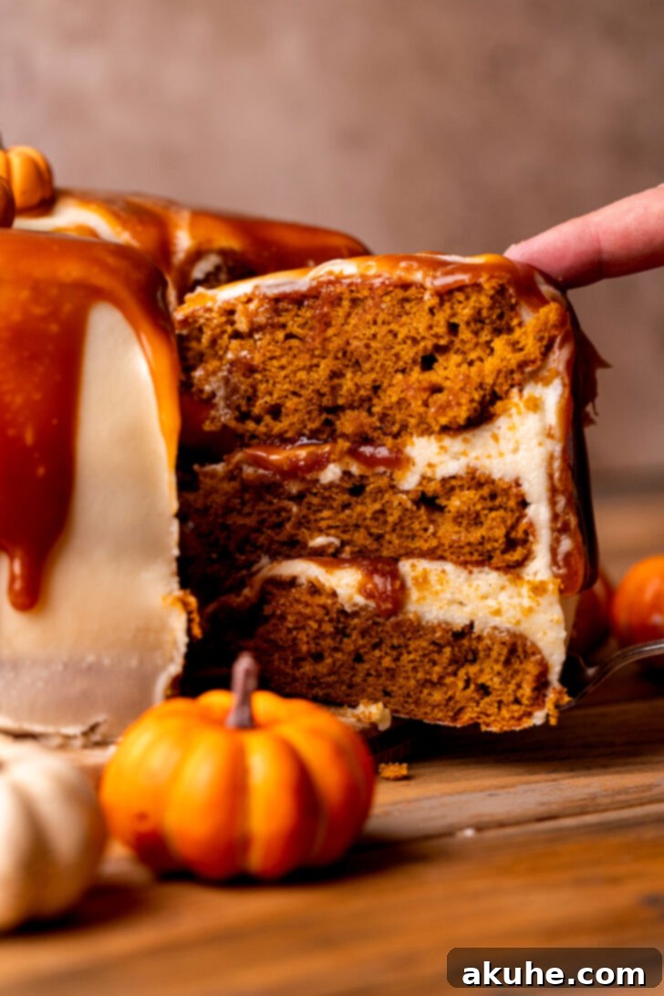 Spiced Pumpkin Caramel Cake 3 A slice being carefully removed from the pumpkin caramel cake, revealing the moist interior, creamy frosting, and gooey caramel layers.