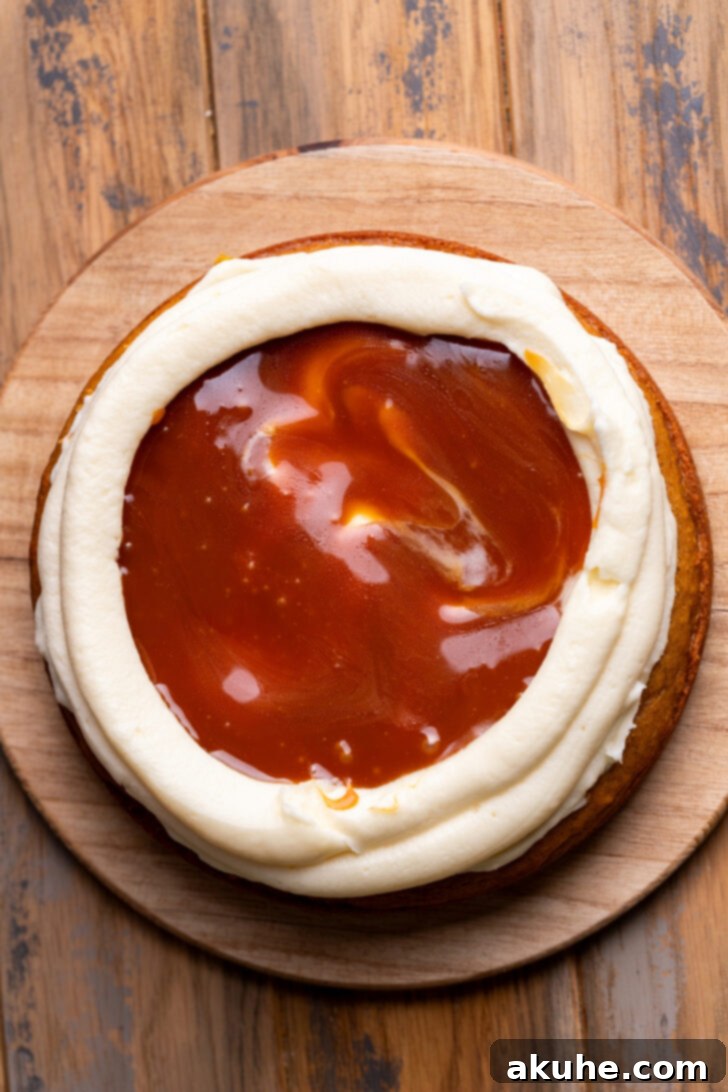 Spiced Pumpkin Caramel Cake 7 Caramel being spread on top of a cake layer with a piped frosting border.