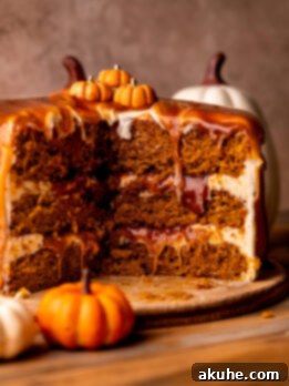 Spiced Pumpkin Caramel Cake 11 Side view of a beautifully assembled pumpkin caramel cake, showing its distinct layers of soft pumpkin cake, maple cream cheese frosting, and salted caramel filling, topped with a caramel drip.