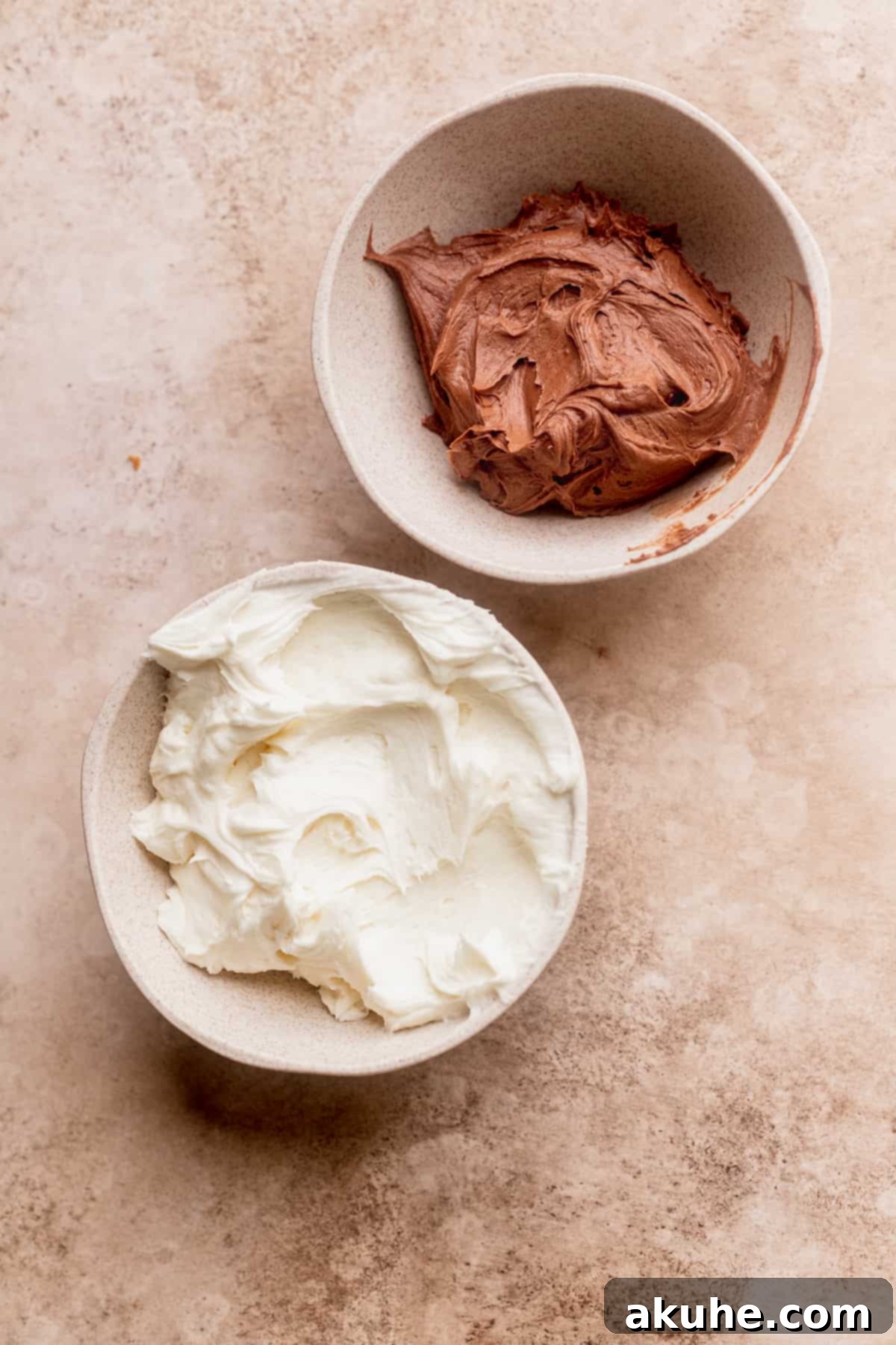 Two bowls brimming with creamy frosting – one plain, one chocolate – ready for swirling onto the cake.