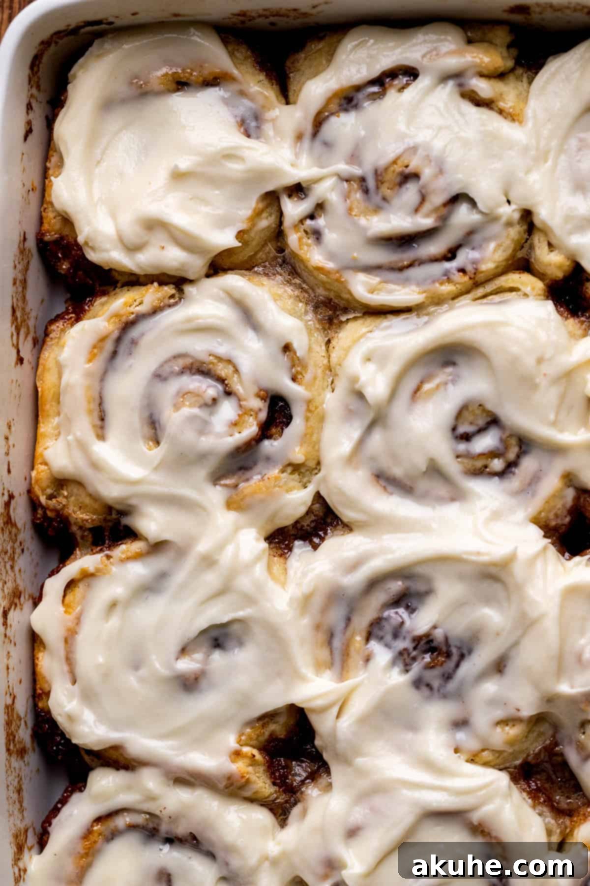 Top view of freshly baked no yeast cinnamon rolls in a square pan, glistening with cream cheese icing.