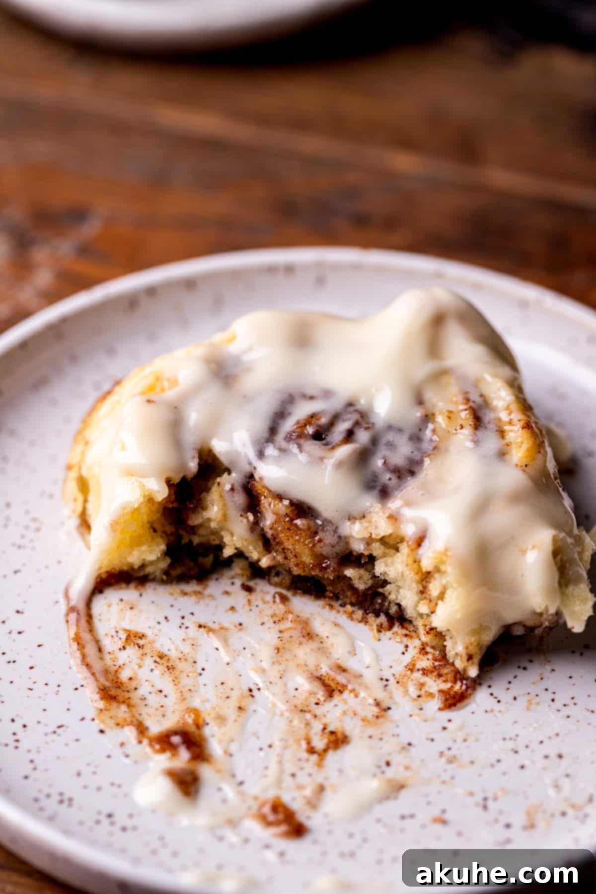 One perfectly frosted no yeast cinnamon roll on a white plate, ready to be eaten.