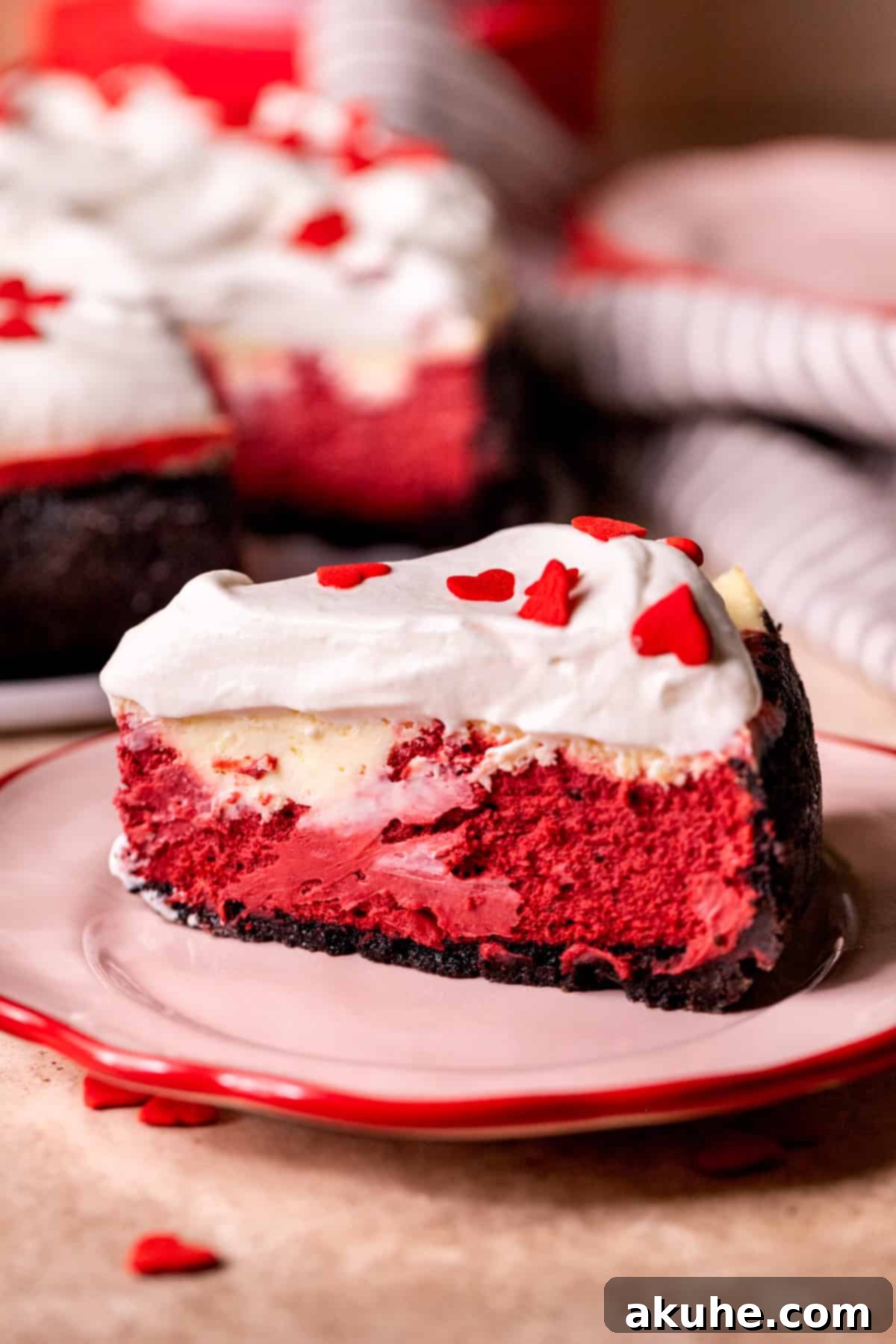 Red Velvet Decadence 12 Close-up side view of a sliced red velvet cheesecake, showcasing its layers and whipped cream.