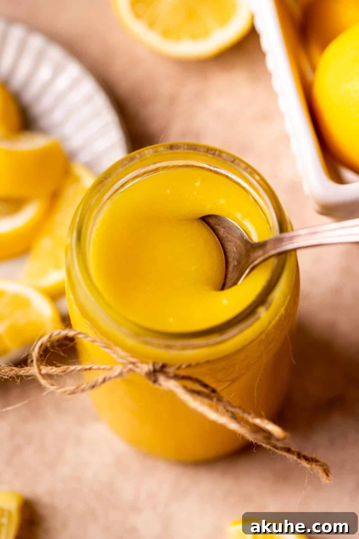A spoon gracefully lifts a scoop of creamy lemon curd from a glass jar, perfectly showcasing its thick and smooth consistency, ready for serving.