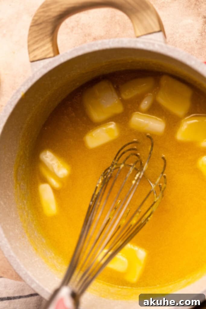 Cold, cubed pieces of unsalted butter are carefully added to the warm, thickened lemon curd in a saucepan, about to be incorporated for a smooth finish.