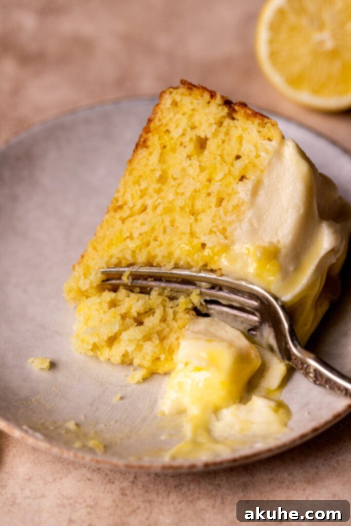 A single slice of lemon curd cake lying on its side, revealing the moist cake, frosting, and curd layers.