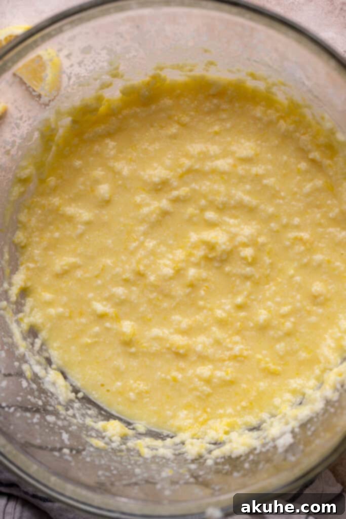 Wet ingredients for lemon cake in a glass mixing bowl, appearing slightly curdled.