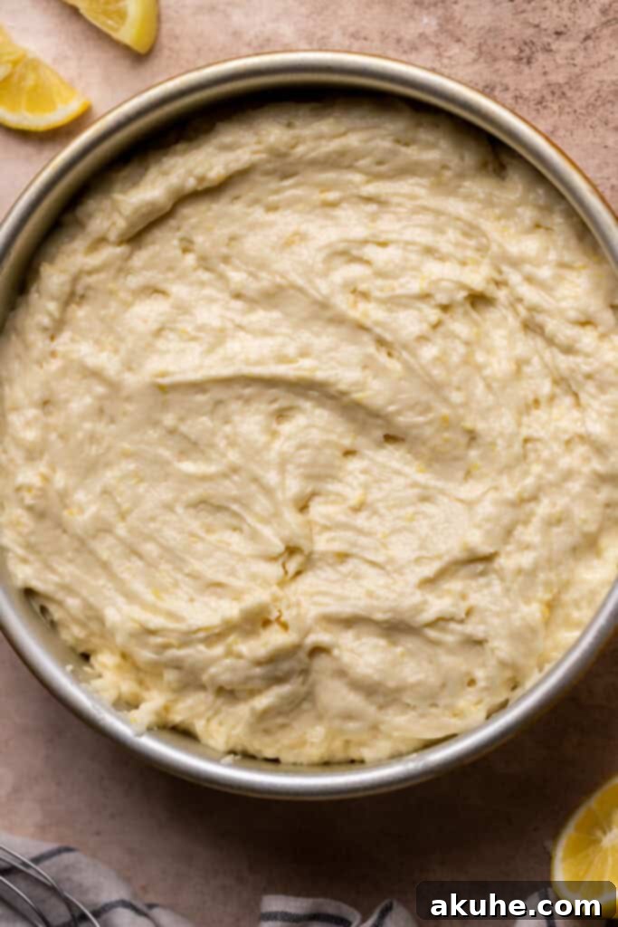 Lemon cake batter evenly spread in a round baking pan, ready for the oven.