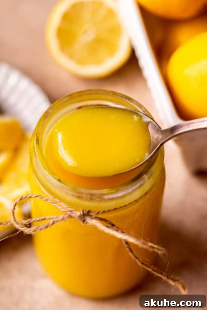 A spoon scooping vibrant yellow homemade lemon curd from a glass jar.
