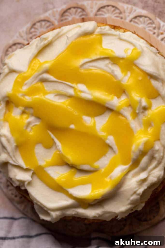 Dollops of bright yellow lemon curd being placed on a cake already covered with white cream cheese frosting.