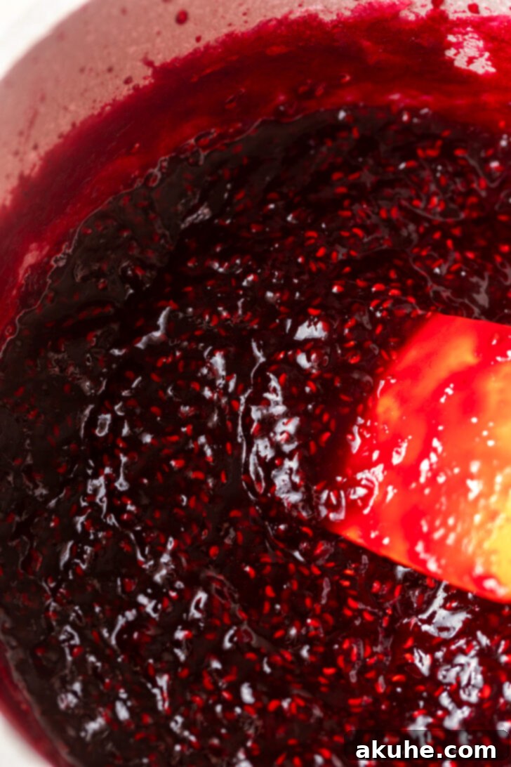 Effortless Raspberry Preserve 6 Thickened raspberry jam simmering in a pot on the stovetop, showing its rich consistency.