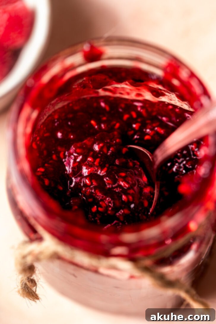 Effortless Raspberry Preserve 8 Close-up of vibrant raspberry jam in a small glass jar, highlighting its rich color and texture.