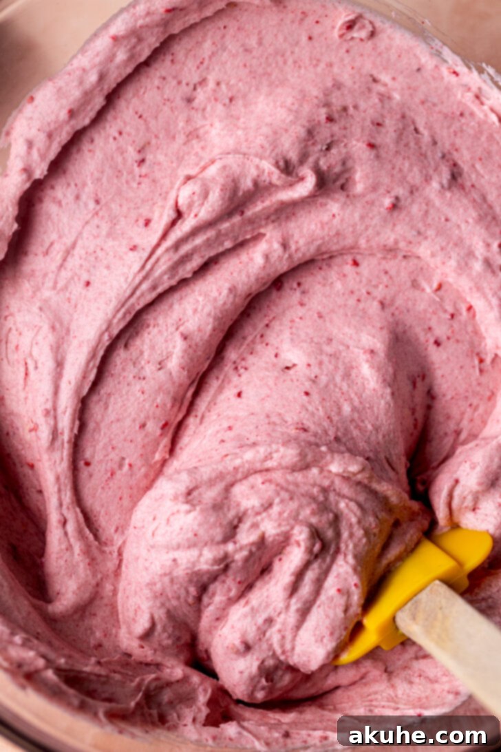 Close-up of fluffy, pink raspberry frosting in a mixing bowl, showcasing its smooth and creamy texture.