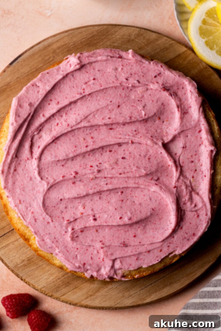 A beautifully frosted cupcake topped with a swirl of creamy raspberry frosting and garnished with fresh raspberries.