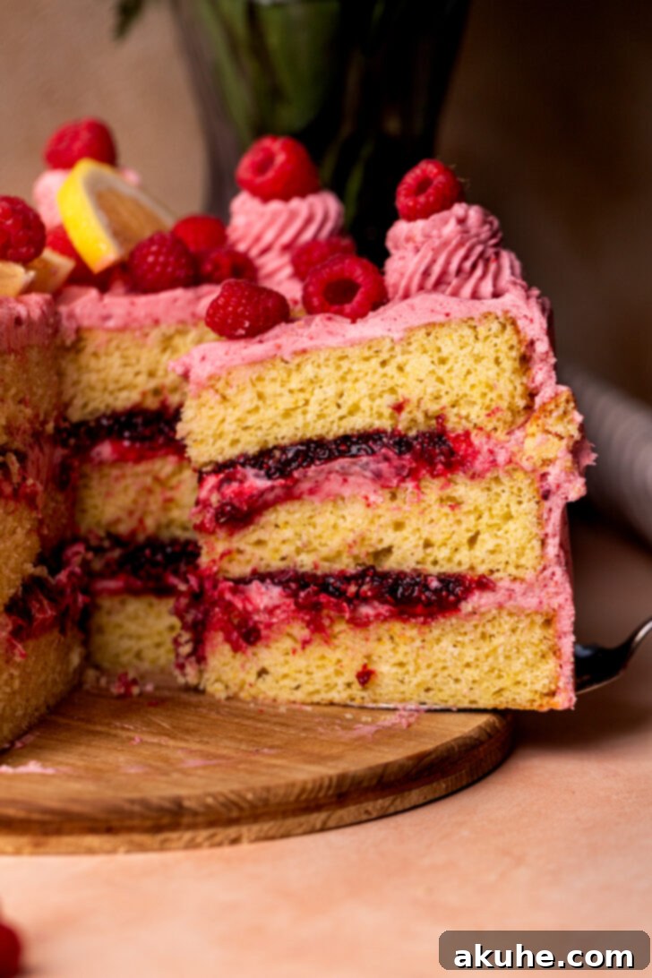 Close-up side view of a slice of lemon raspberry cake, showing the perfect layers of cake, jam, and frosting.