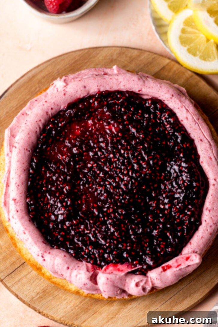 Raspberry jam being spread within a piped frosting border on a cake layer.