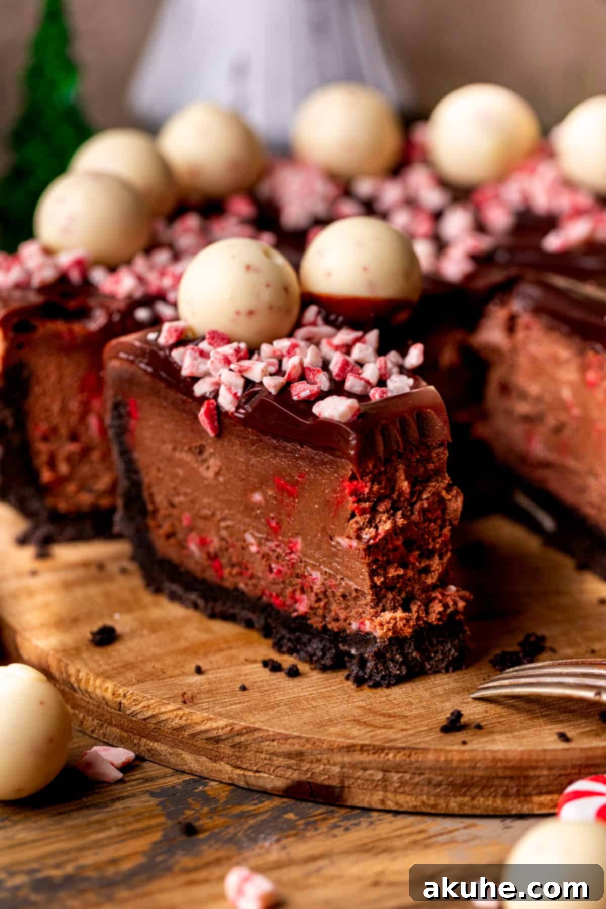 Peppermint Bark Cheesecake 2 A perfectly sliced piece of chocolate peppermint cheesecake resting on a rustic wooden board, showcasing its rich layers and festive toppings.