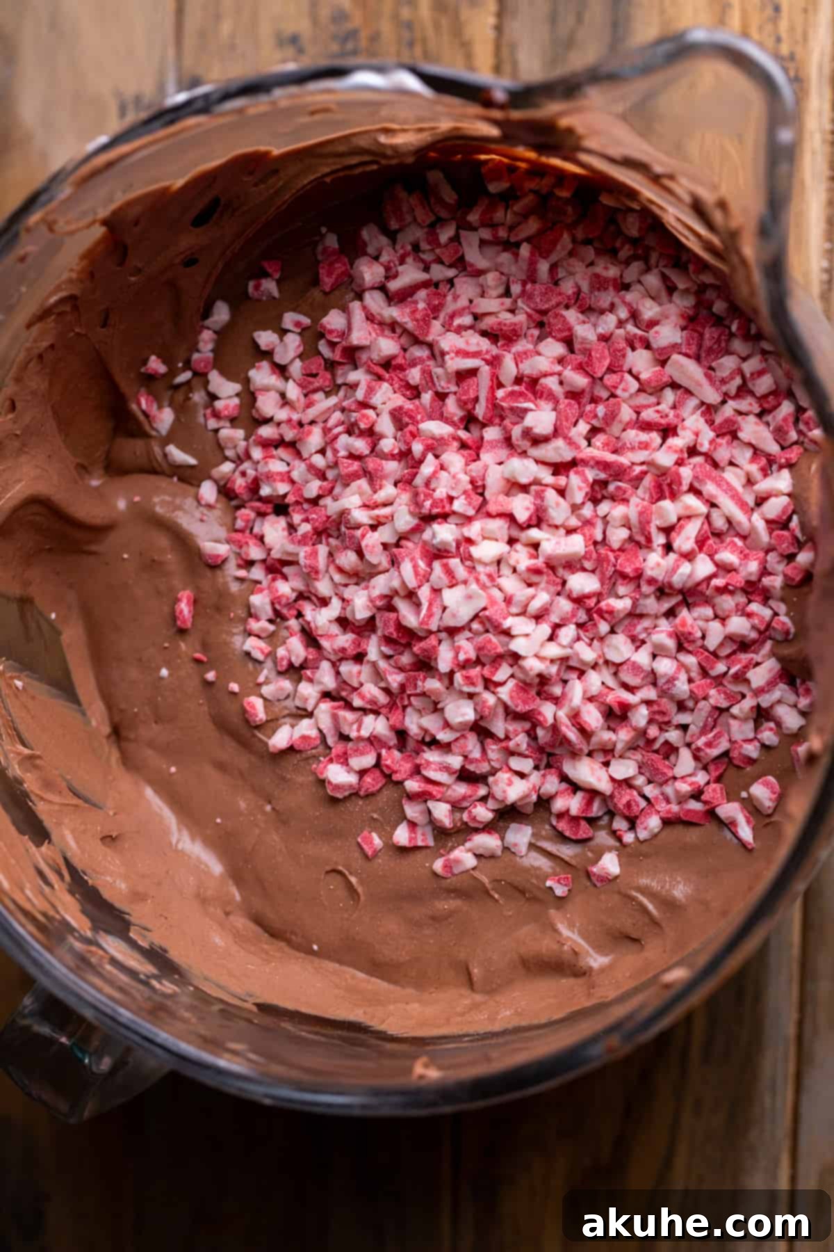 Peppermint Bark Cheesecake 5 Close-up view of peppermint chips being folded into the smooth chocolate cheesecake batter in a mixing bowl.