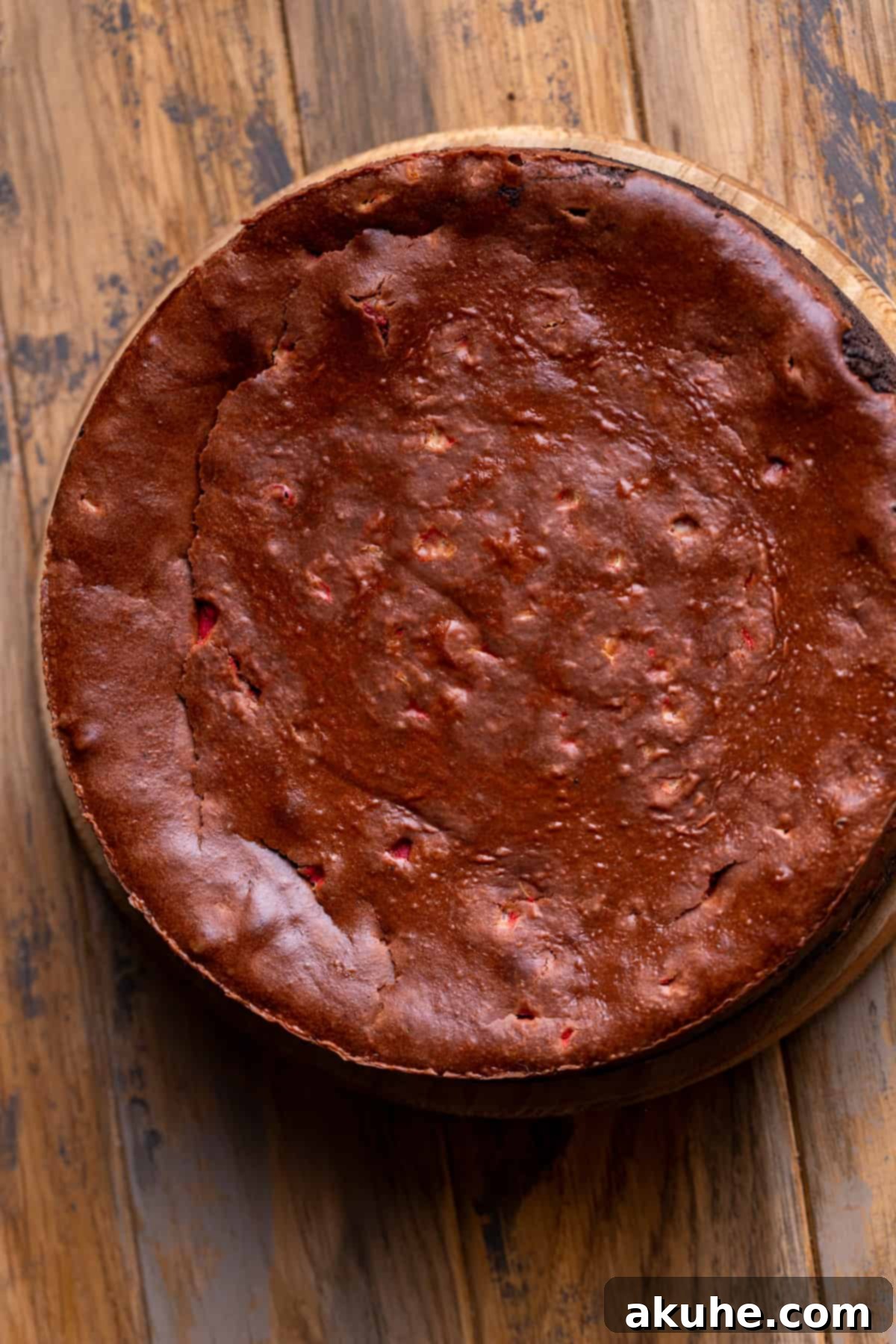 Peppermint Bark Cheesecake 8 A perfectly baked chocolate cheesecake, golden-brown and set, cooling on a wooden board.
