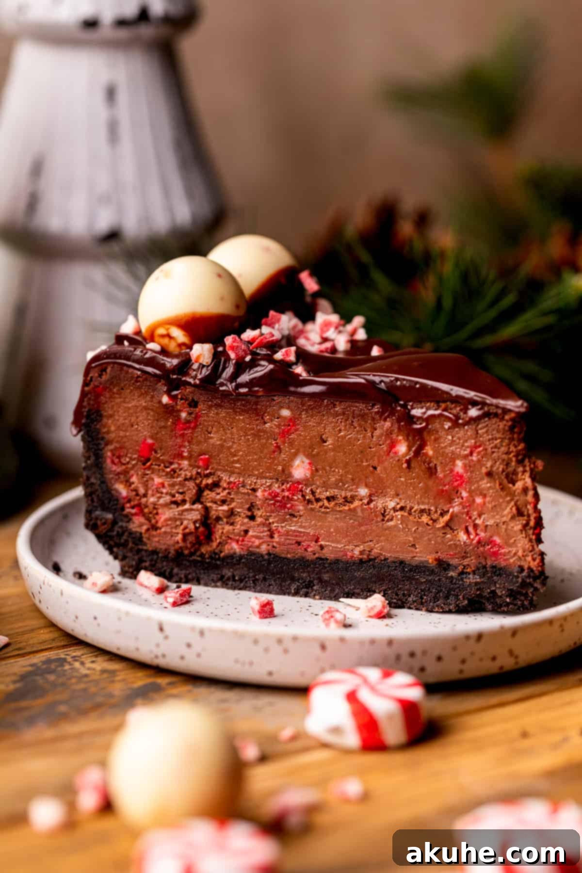 Peppermint Bark Cheesecake 10 A single, delectable slice of chocolate peppermint cheesecake, adorned with ganache and peppermint chips, on a plate.