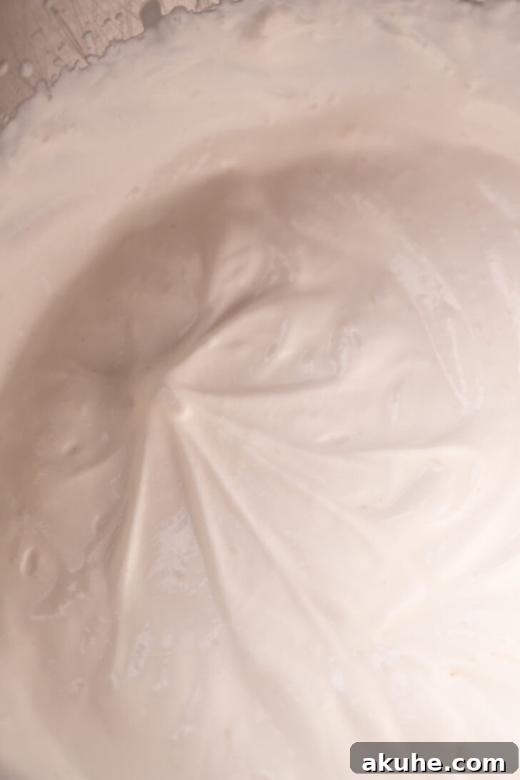 Rich Mascarpone Icing 5 Whipped heavy cream showing distinct soft peaks on the beater, indicating the correct stage of whipping.