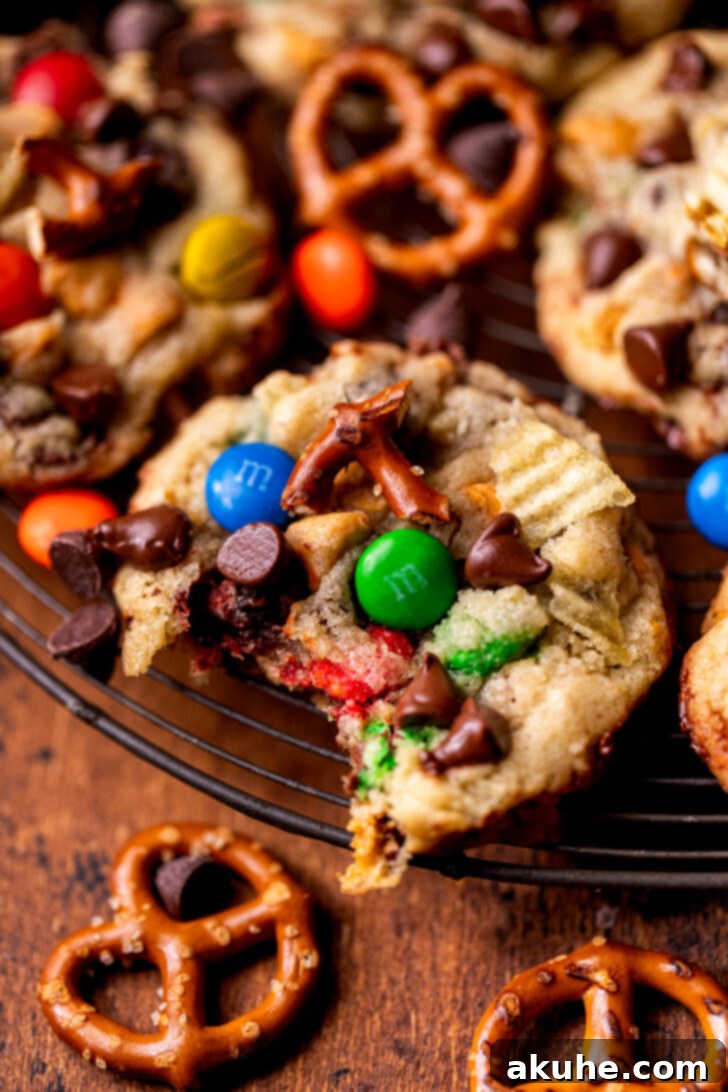 The Everything Cookie 3 A Kitchen Sink Cookie with a bite taken out, revealing its soft, chewy interior and the assortment of mix-ins like chocolate, pretzels, and potato chips.