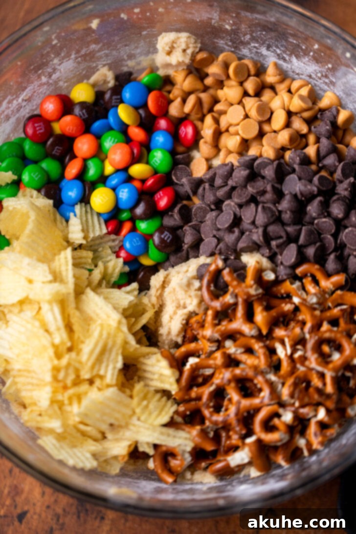 The Everything Cookie 5 Cookie dough balls on a baking sheet with extra chocolate chips and M&M's pressed onto their tops before baking.