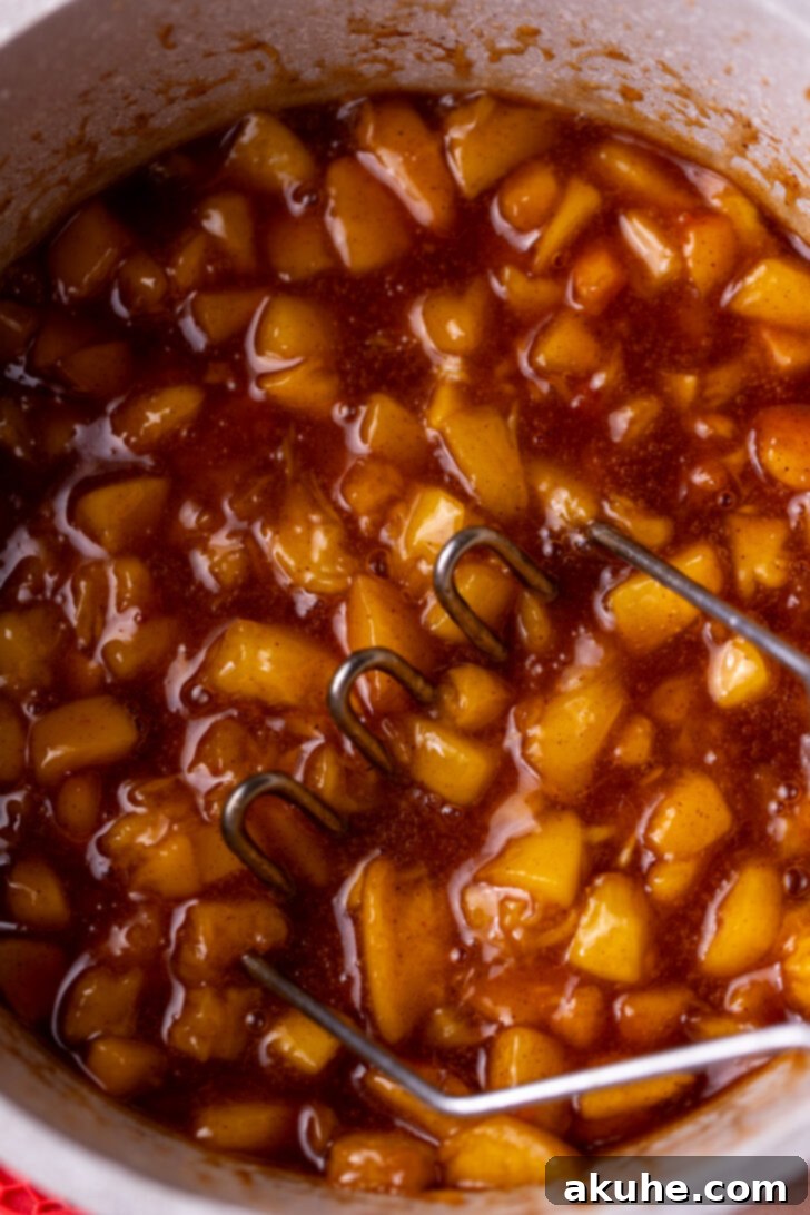 Classic Peach Pie Filling 6 Peach filling being mashed with a potato masher in a saucepan.