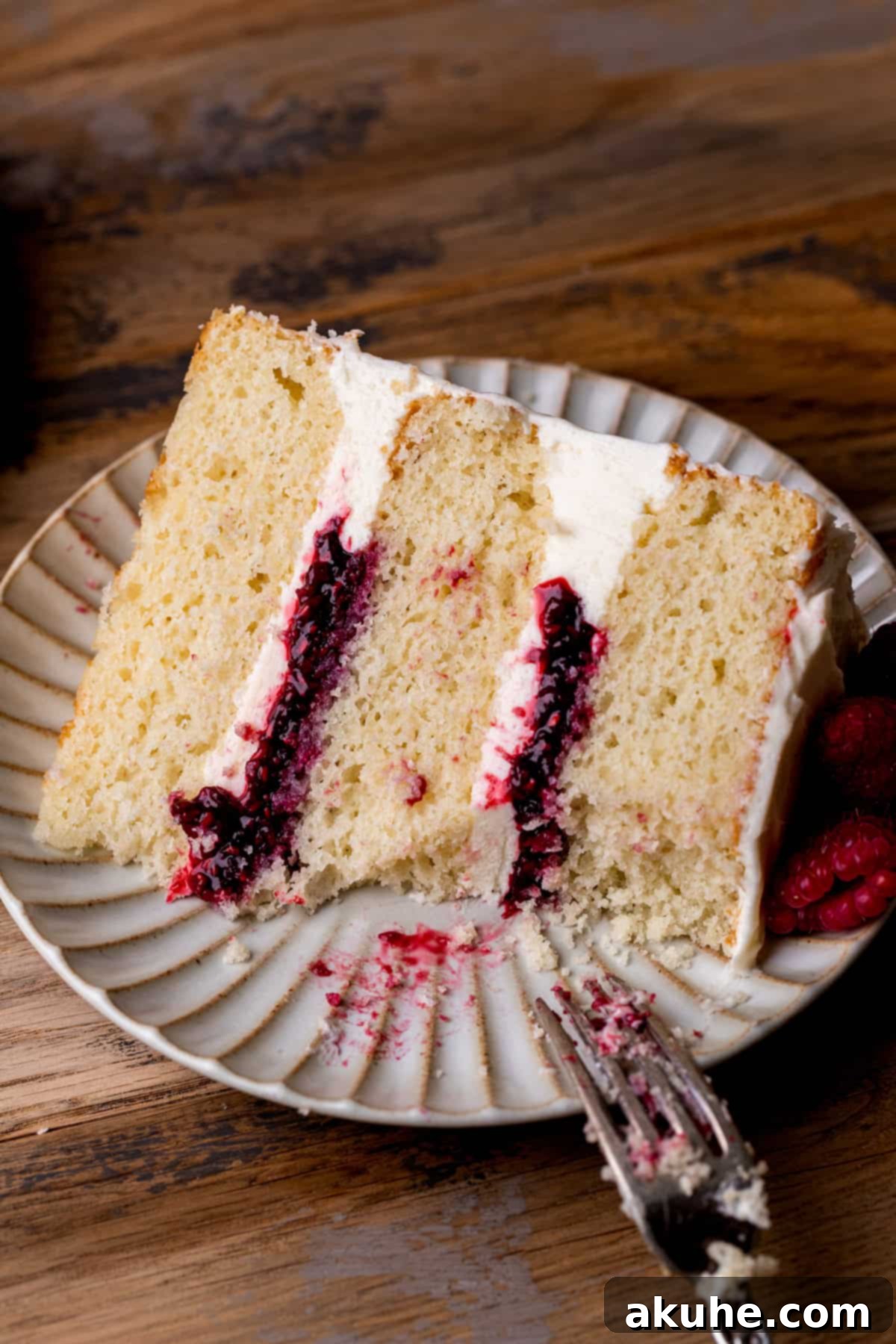 A slice of white chocolate raspberry cake with a bite missing, showing off the beautiful layers and filling.