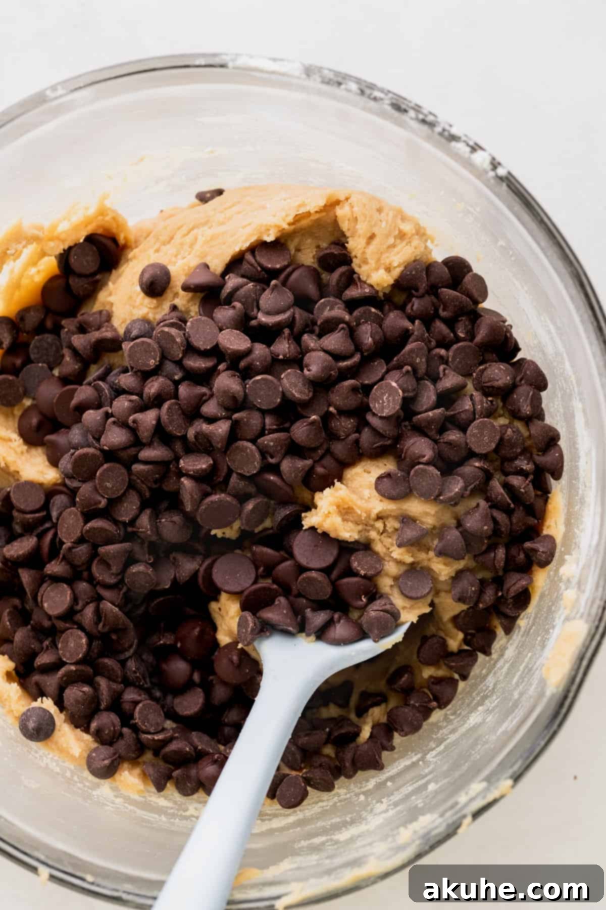 Ultimate Chocolate Chip Cookies 5 A generous amount of chocolate chips added to the freshly mixed cookie dough in a glass bowl.