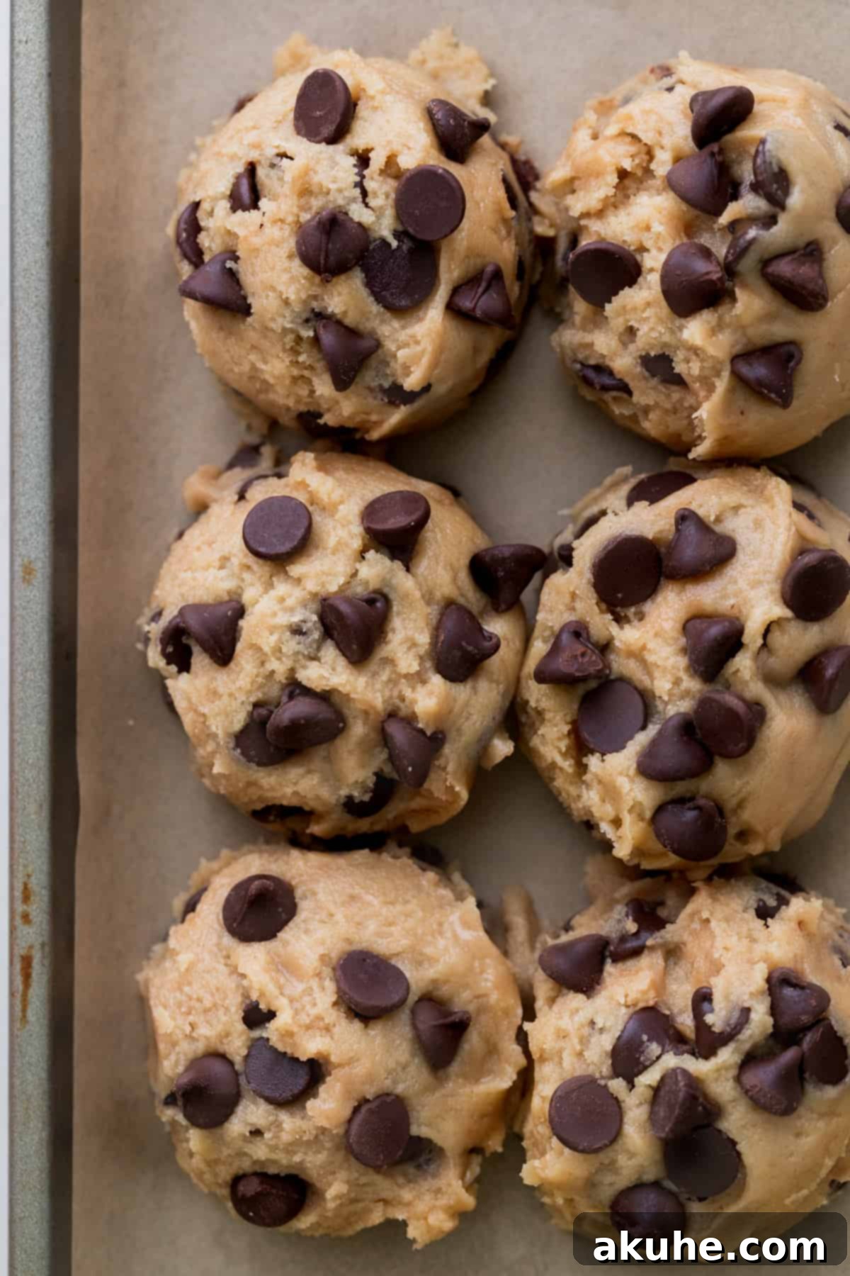 Ultimate Chocolate Chip Cookies 7 Six large chocolate chip cookie dough balls neatly arranged on a parchment-lined cookie sheet, ready for baking.