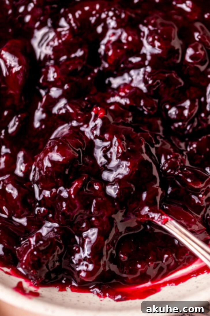 Homemade Cherry Pie Filling 7 A spoon scooping a generous portion of homemade cherry pie filling from a bowl, showcasing its luscious texture and vibrant color.