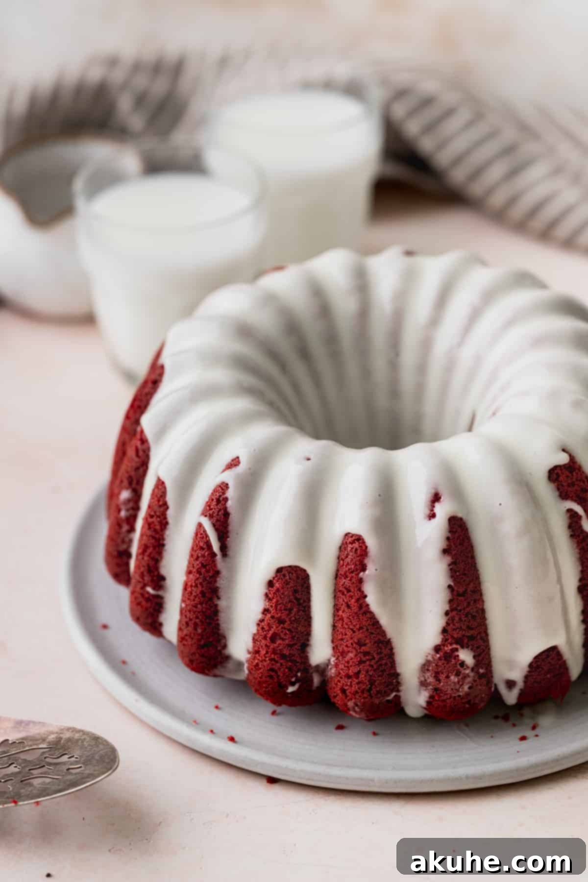 Crimson Crown Bundt Cake 3 A beautifully baked Red Velvet Bundt Cake, generously drizzled with white cream cheese glaze, resting on a serving platter.