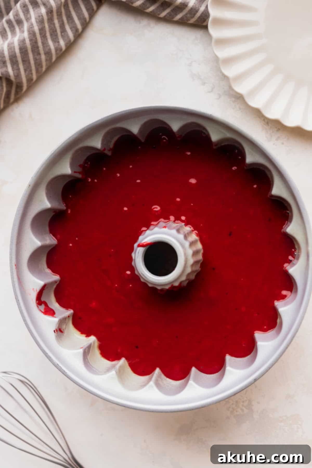 Crimson Crown Bundt Cake 6 Bright red cake batter being carefully poured into a fluted bundt pan, ready for baking.