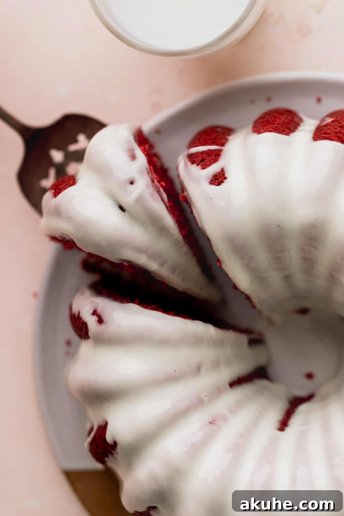 Crimson Crown Bundt Cake 10 A hand gently removing a slice from a freshly glazed Red Velvet Bundt Cake on a wire rack.