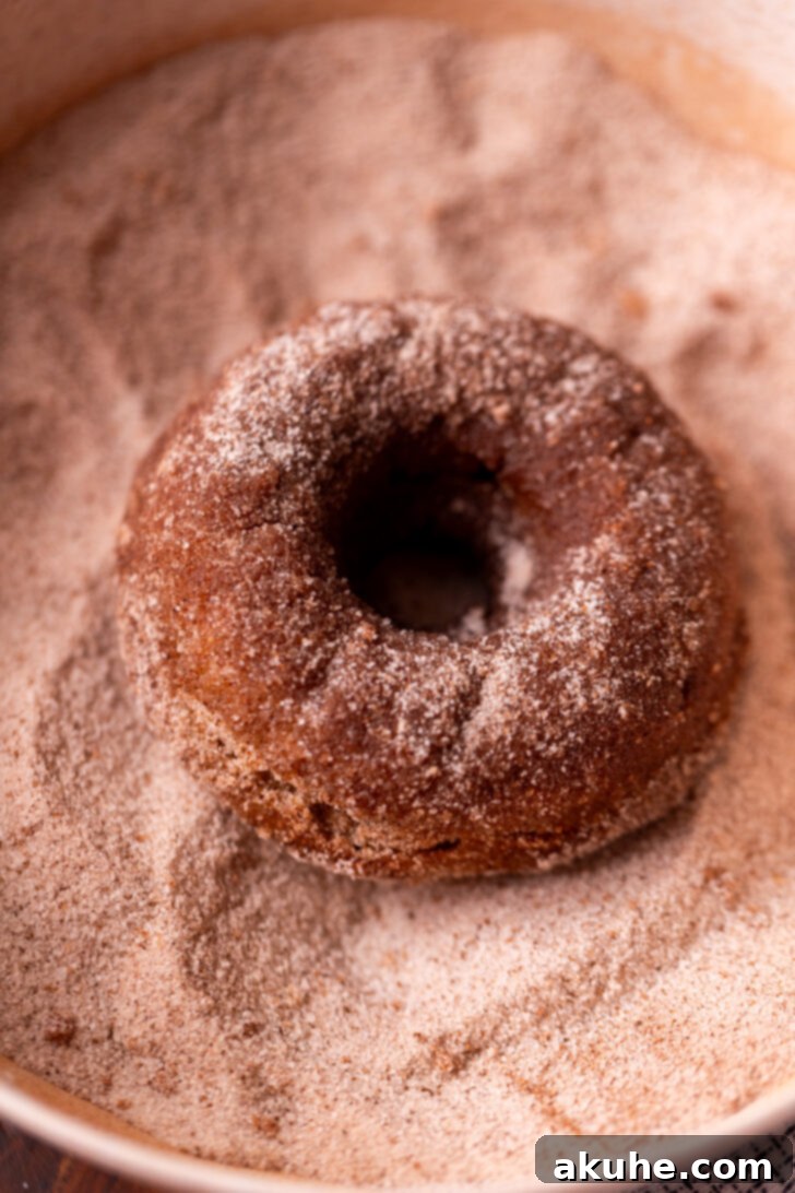 Harvest Apple Cider Donuts 8 A freshly butter-dipped donut being generously tossed in a bowl of cinnamon sugar.