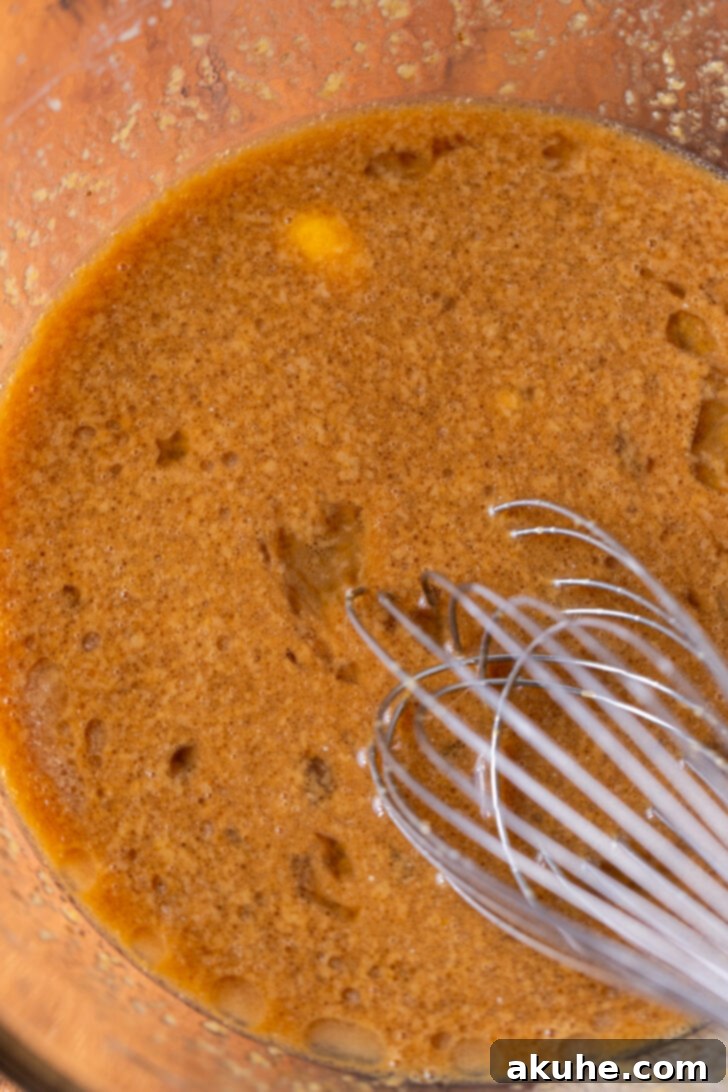 Golden Apple Muffins 5 A bowl containing thoroughly mixed wet ingredients: oil, brown sugar, eggs, vanilla, applesauce, and milk, forming a smooth consistency.