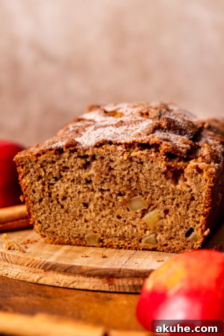 Spiced Apple Bread 3 Side view of a freshly baked cinnamon apple bread loaf resting on a wooden board, ready to be sliced.